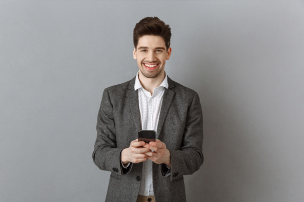 ritratto di un uomo d'affari sorridente con smartphone sullo sfondo grigio della parete
 - Foto, immagini