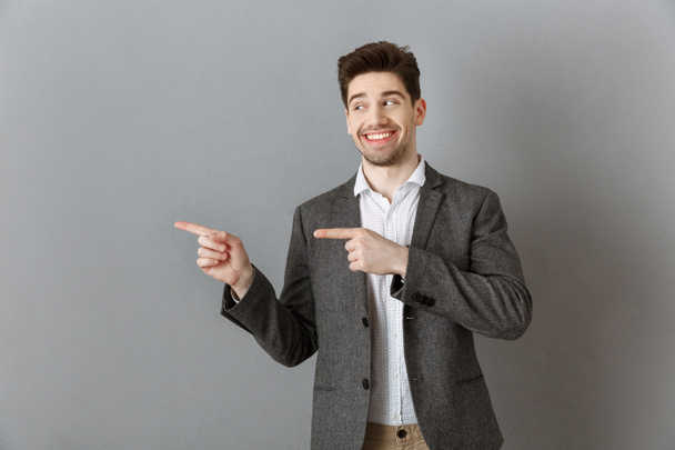 πορτρέτο του χαμογελώντας επιχειρηματία στο κοστούμι δείχνει μακριά γκρίζα τοίχο - Φωτογραφία, εικόνα