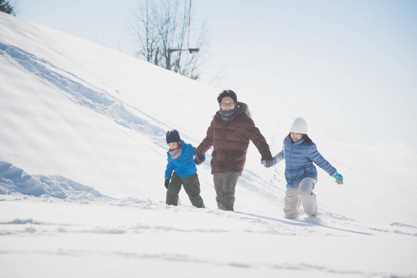 アジアの父と彼の子供たちが手を取り合って、一緒に雪の中を歩く - 写真・画像