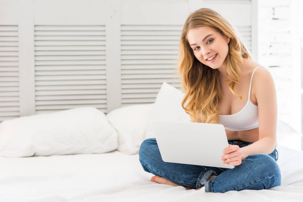 szczęśliwy atrakcyjna dziewczyna za pomocą laptopa siedząc na łóżku - Zdjęcie, obraz