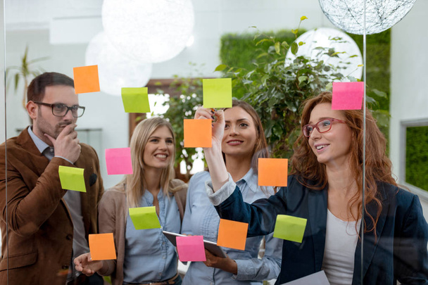 Creative professionals standing in office behind glass wall with sticky notes - Photo, Image