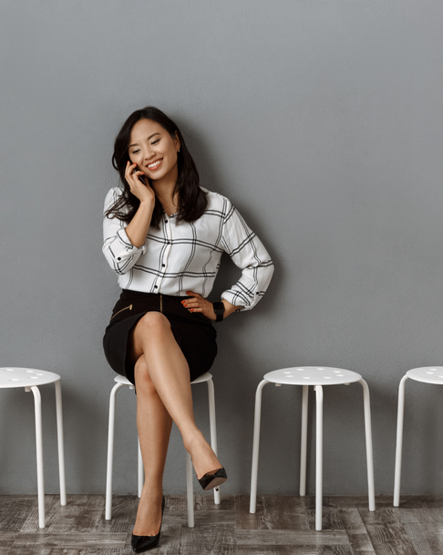 улыбающаяся азиатская бизнесвумен разговаривает по смартфону в ожидании собеседования
 - Фото, изображение