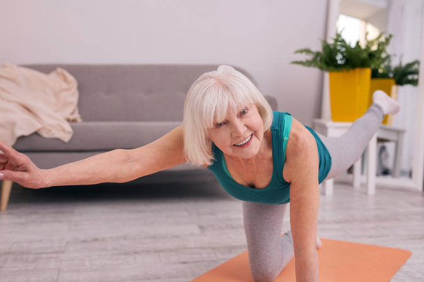 Upbeat elderly woman doing stretching while standing on one knee - Fotó, kép