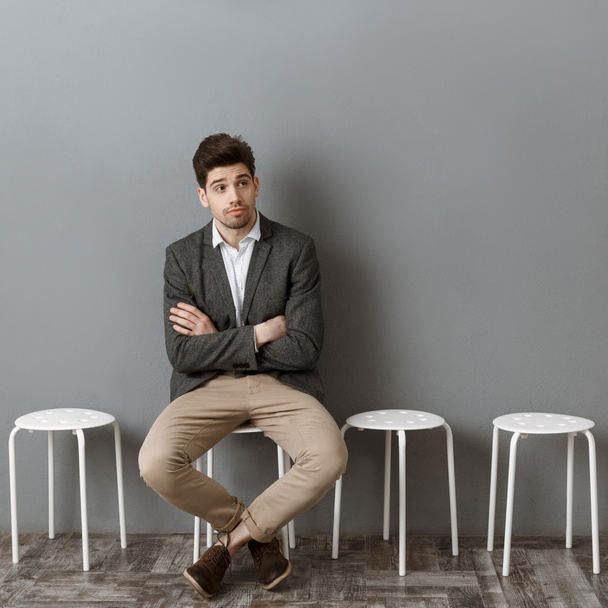 uomo d'affari pensieroso in attesa di un colloquio di lavoro sulla sedia contro il muro grigio
 - Foto, immagini