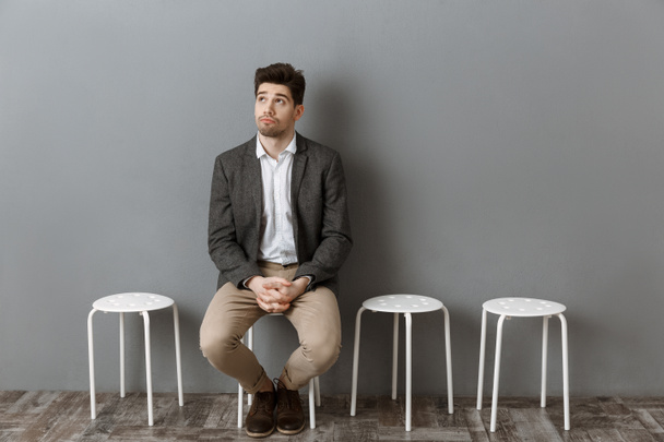 empresario pensativo a la espera de entrevista de trabajo en silla contra la pared gris
 - Foto, imagen