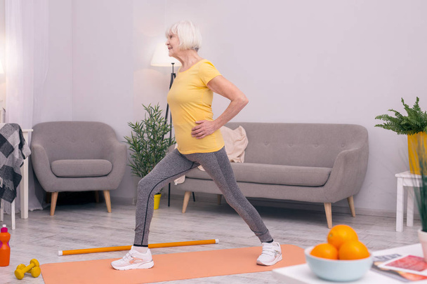 Athletic senior woman performing lunges in the living room - Foto, afbeelding