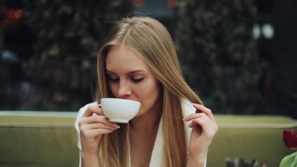 Adorable young woman drinks her coffee sitting in the cafe - Filmati, video