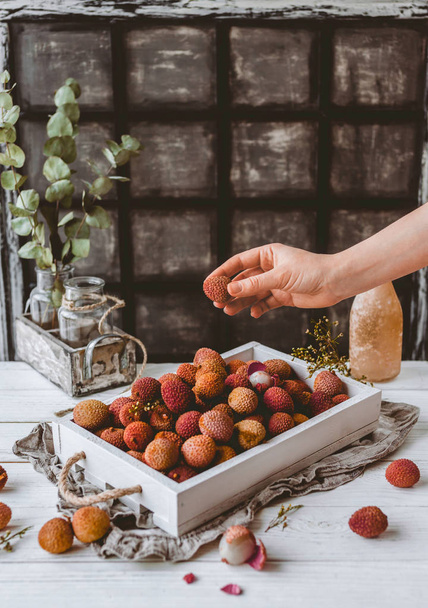 cropped image of female hand and pile of lychees in wooden box on table - Фото, зображення
