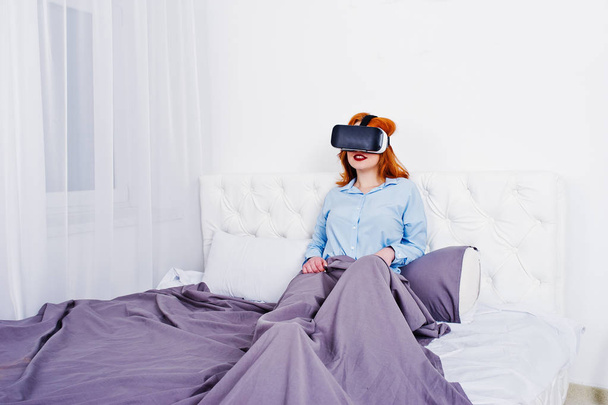 Red haired girl in bed with vr glasses at studio room. - Фото, изображение