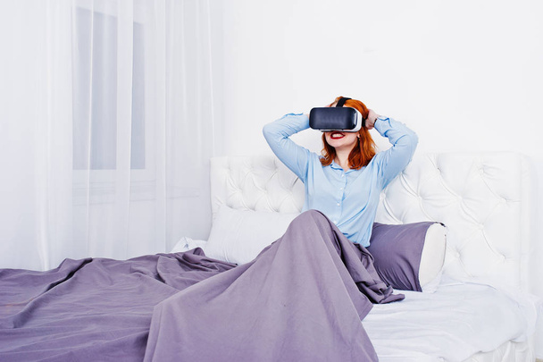 Red haired girl in bed with vr glasses at studio room. - Photo, image