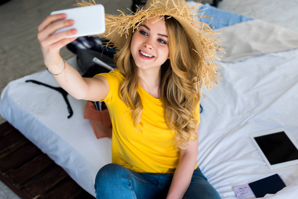 attractive smiling girl in straw hat taking selfie on smartphone - Photo, image