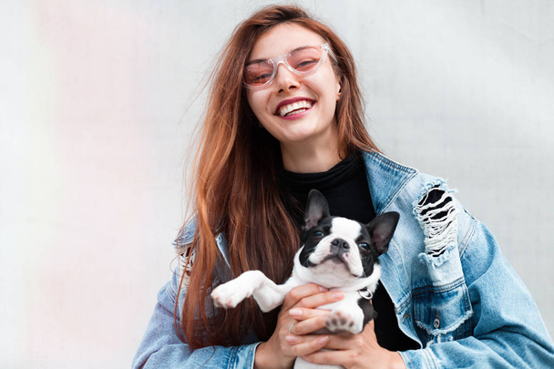 Portrait of woman with dog.young happy woman with little cute puppy boston terrier.Cheerful young woman in trendy jeans coat.holding her french bulldog puppy,laughing.concept about animals and people. - Photo, Image