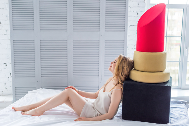 mooie blonde jonge vrouw poseren met grote rode lippenstift in slaapkamer - Foto, afbeelding