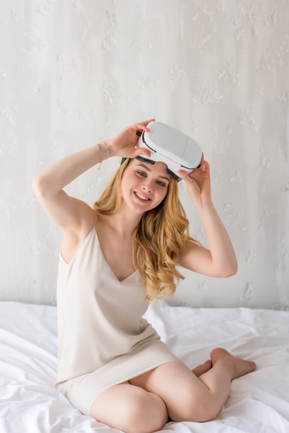 smiling woman using virtual reality headset in bedroom - Fotó, kép