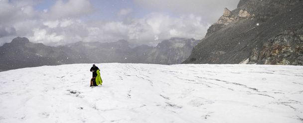 alpinista wplątuje się w złych warunkach pogodowych i stawia na więcej ubrań, jak on stoi na wysoki alpejski lodowiec z widok z restauracji - Zdjęcie, obraz