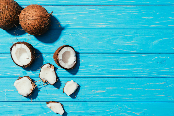 top view of whole coconuts and pieces on turquoise wooden surface  - 写真・画像