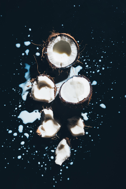 close-up view of pieces of healthy coconuts and organic coconut milk on black  - Фото, изображение