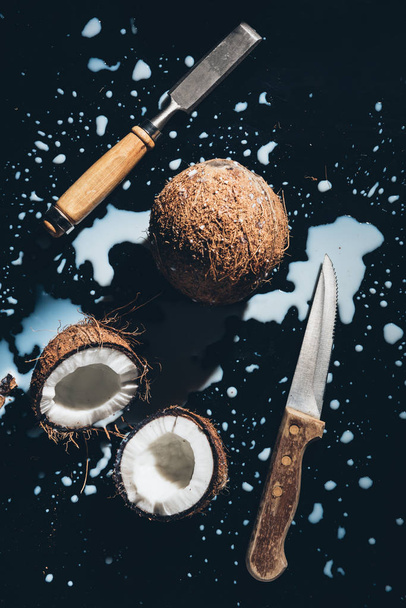 Widok z góry kokosy, dłuta, nóż i mleko kokosowe na czarny  - Zdjęcie, obraz