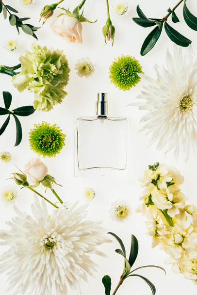 top view of glass bottle of perfume surrounded with flowers and green branches isolated on white - Фото, зображення