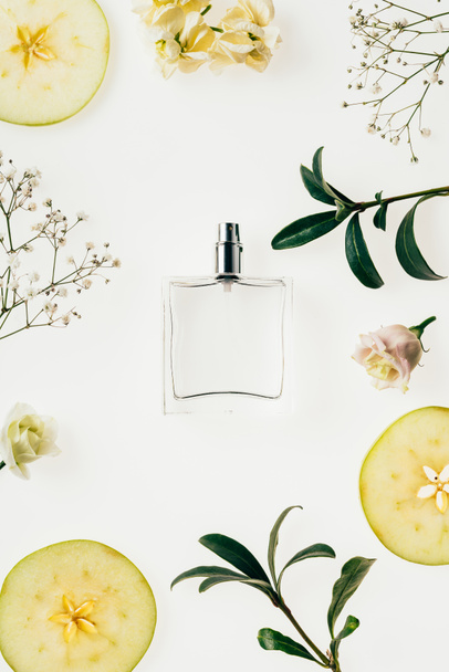 top view of bottle of perfume surrounded with flowers and apple slices isolated on white - Φωτογραφία, εικόνα