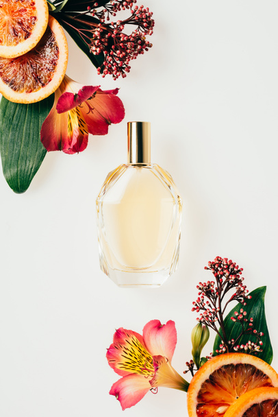 vista superior de la botella de vidrio de perfume aromático con varias flores y rodajas de pomelo aisladas en blanco
 - Foto, Imagen