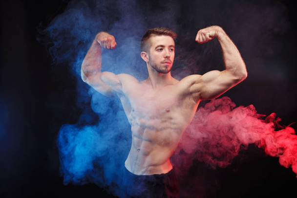 Bodybuilder man with perfect muscles in blue and red smoke - Фото, зображення