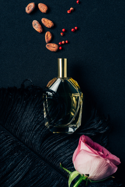 top view of bottle of perfume with rose bud and spices on black - Фото, изображение