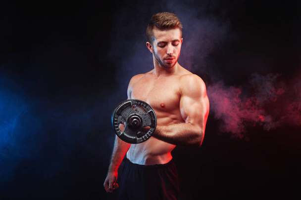 Muscular bodybuilder guy doing exercises with dumbbell over blac - Fotografie, Obrázek
