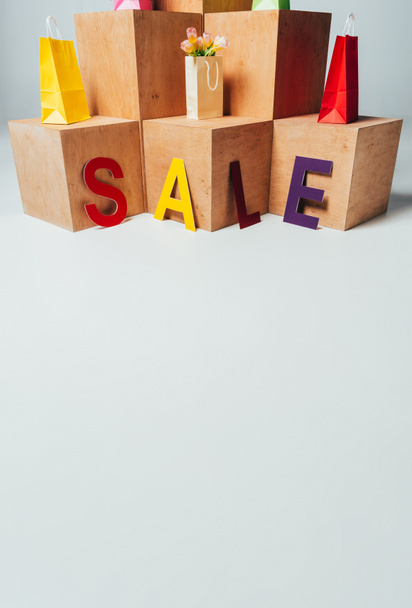 colored paper bags on wooden stands with sale sign, summer sale concept - Foto, Imagem