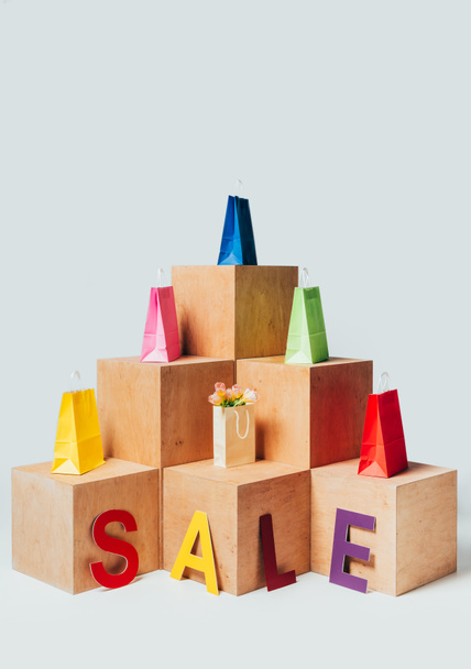 colored shopping bags on wooden stands with sale sign isolated on white, summer sale concept - Photo, image