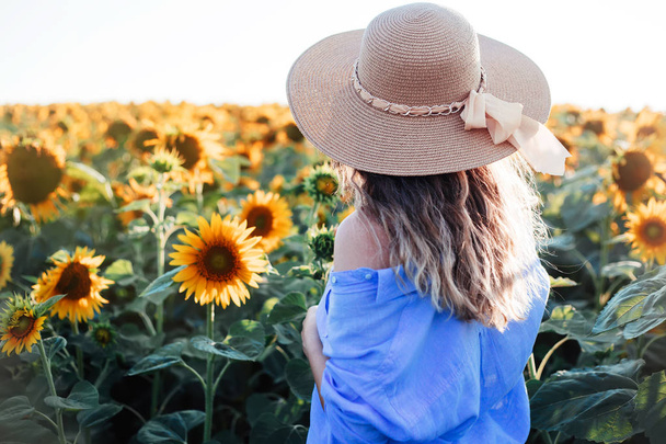 Young woman walking in the field with sunflowers.Beautiful young girl enjoying nature on the field of sunflowers at sunset.woman with long hair , back view. The concept of freedom.Sunflower background - Fotó, kép