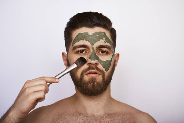 Closeup beauty image of Young man with green clay on the face on gray background - Fotoğraf, Görsel