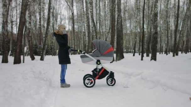 Bir bebek arabası ile yürüyen genç bir anne yan görünüm - Video, Çekim