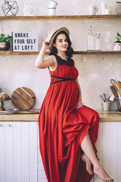 Fashion portrait of attractive stylish pregnant lady in long red sarafan and straw hat, photo of the happy and beautiful pregnant woman, becoming parrents, stylish clothes for pregnancy, future mother - Foto, Bild