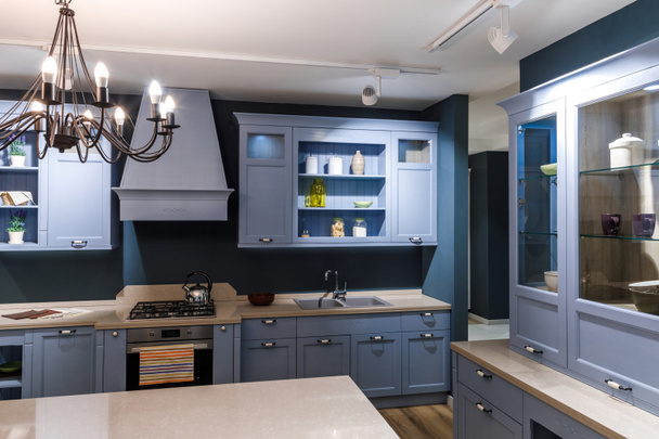 Stylish kitchen in blue tones with elegant chandelier - 写真・画像