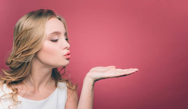 Pretty young woman is posing. She has closed her eys and put her lips together in a kiss shape. She is sending some kisses. Isolated on pink background. - Fotografie, Obrázek