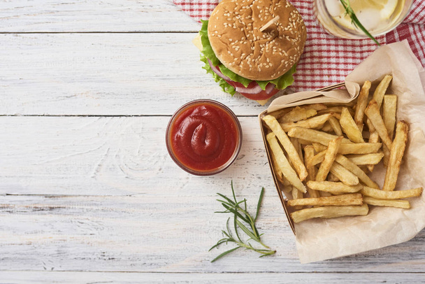 Concept of picnic. Tasty fresh burgers, french fries and two glasses with lemonade on red kitchen towel over white rustic wooden background. - Photo, Image