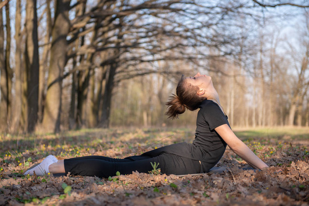 Urdhvamukha shvanasana. A girl in black clothes is engaged in yoga on a natural background - Foto, Imagem
