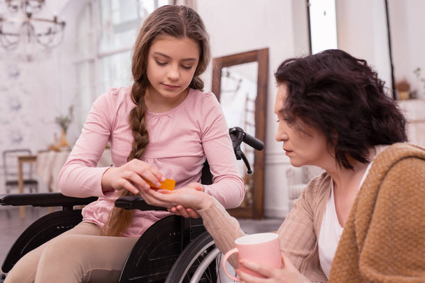 Earnest handicapped girl giving pills to woman - Fotoğraf, Görsel