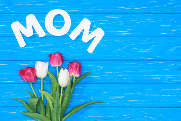 top view of bouquet of pink and white tulips and word mom on blue table, mothers day concept - Photo, Image