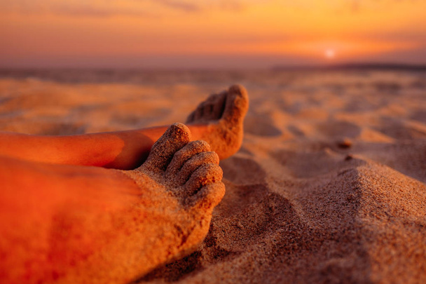 View of female barefoot legs on beach sand at sunset.  - Foto, afbeelding