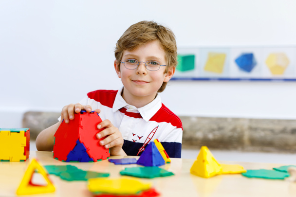 Щасливий хлопчик в окулярах розважається з будівництвом і створює геометричні фігури, вивчає математику і геометрію
 - Фото, зображення