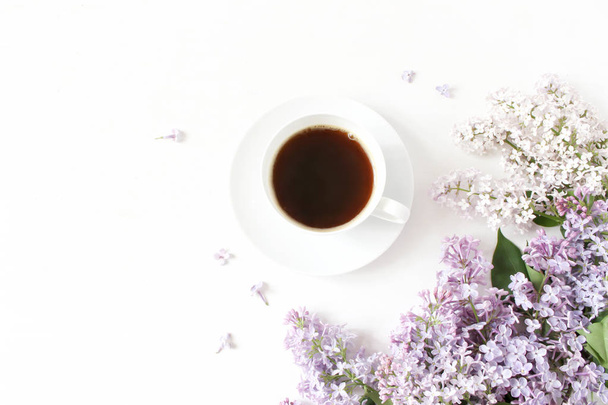 Floral composition made of beautiful purple lilac, syringa flowers on white wooden background with cup of coffee. Feminine office desk, styled stock image, flat lay, top view with empty space. - Fotoğraf, Görsel
