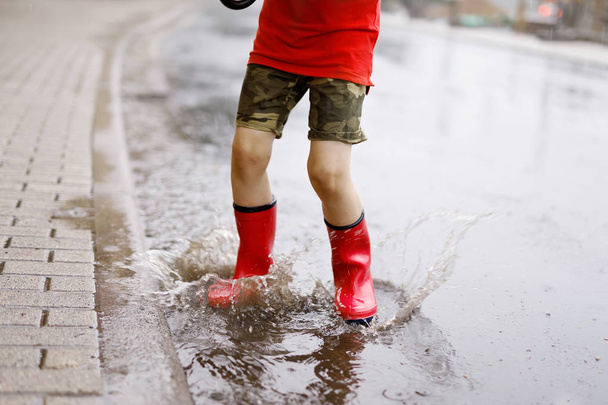 παιδί φορώντας κόκκινο βροχή μπότες άλμα σε μια λακκούβα. - Φωτογραφία, εικόνα