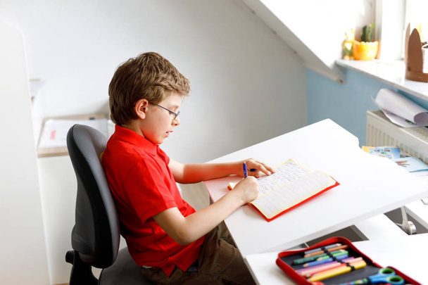 niedliche kleine Junge mit Brille zu Hause Hausaufgaben machen, Schreiben von Briefen mit bunten Stiften. - Foto, Bild