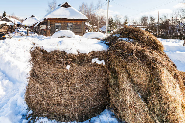 村の雪に覆われた通りに干し草の山 - 写真・画像