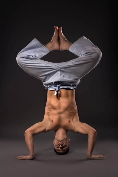 Η μυώδης άνδρας κάνει ένα handstand σε γκρίζο φόντο  - Φωτογραφία, εικόνα