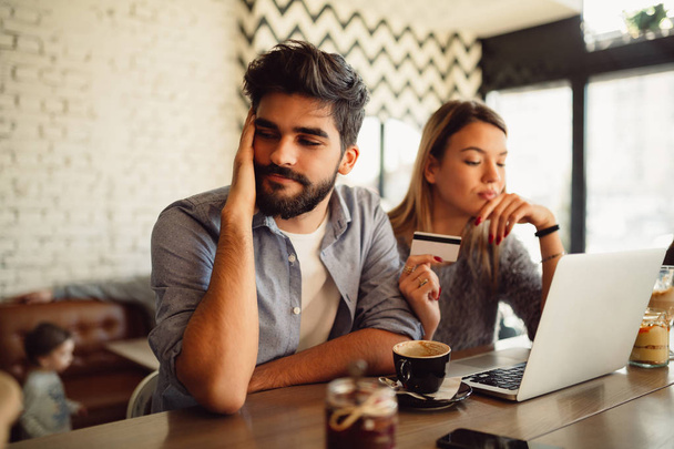 Young couple with notebook and credit card drinking coffee in cafe - Photo, image