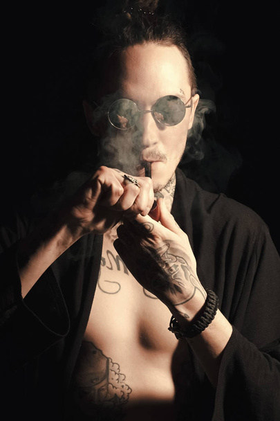 Guy smoker in sunglasses and open clothes showing tattooed torso - Фото, зображення