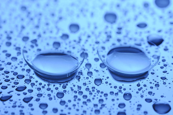 Two contact lenses with drops on light background. Blue toned image. Concept sight. - Foto, imagen
